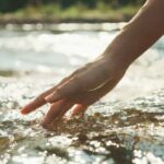 Une main effleurant la surface d’une rivière, l’eau s’écoulant doucement autour des doigts.